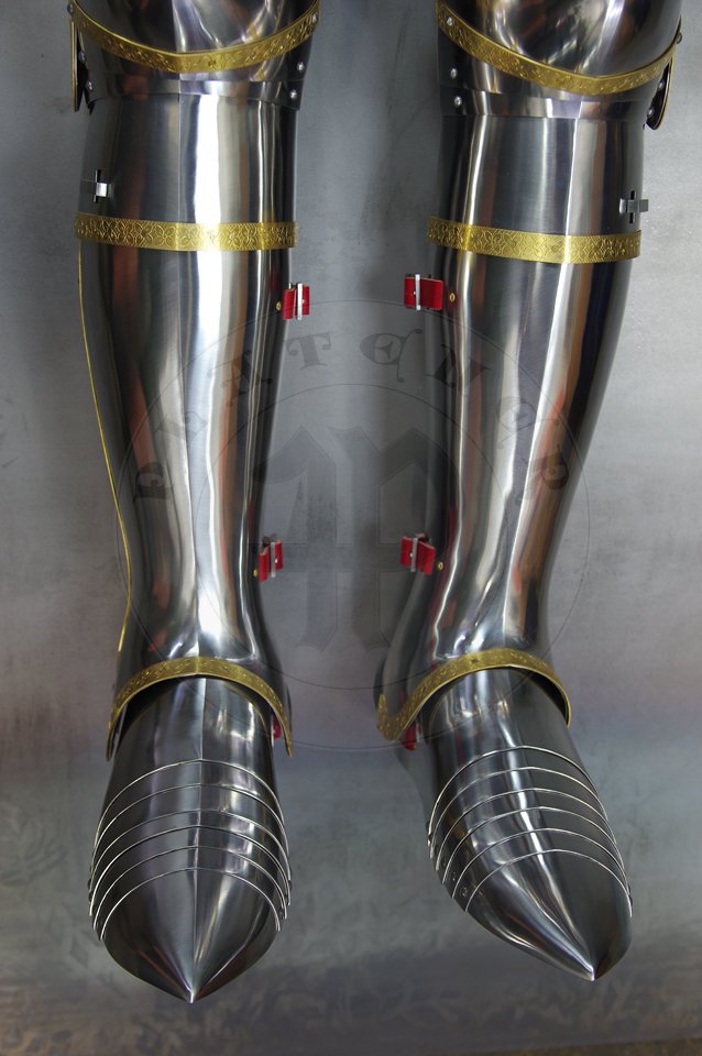 English style leg harness with fully closed cuisses, full greaves with characteristic line around outside ankles. Demi-greaves connected with greaves on rotary pin. Made of medium carbon steel of various thickness from 1 mm up to 1,5 mm. Heat hardened and tempered up to 42 HRC. Brass bands decoration motive based on example visible on Henry V tournament helm. Hand made steel buckles in set./Osony ng w stylu angielskim z w peni zamknitymi nabiodrkami, nagolennicami z charakterystyczn lini wok zewntrznej kostki. Demi-greave poczony z nagolennicami poprzez obrotowy pin. Wykonane ze stali redniowglowej rnej gruboci od 1 mm do 1,5 mm. Hartowane i odpuszczane do 42 HRC. Mosine listwy dekoracyjne z motywem wzorowanym na hemie turniejowym Henryka V. W zestawie rcznie robione sprzczki stalowe.